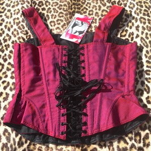 May include: A magenta corset top with black lacing and straps. The top has a textured fabric and a peplum-style hem. A tag with the text "LA DOUCHKA VINTAGE" is attached. The corset is displayed on a leopard print background.