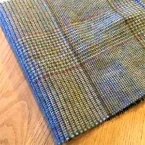 May include: A close-up of a woven fabric with a checkered pattern in shades of blue, green, and brown. The fabric has a soft, textured feel.