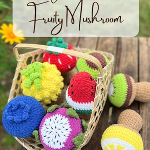 May include: A woven basket filled with colorful crocheted fruit-shaped toys. The basket contains a strawberry, avocado, watermelon, kiwi, pineapple, blueberry, dragon fruit, and a mushroom. The text "Fruity Mushroom" is at the top.