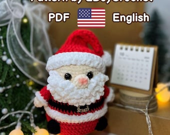 May include: A crocheted Santa Claus figure with a red hat and suit, white beard and trim, and black belt. The text "Pattern by 2BoyCrochet PDF English" is visible. A small calendar and string lights are in the background.