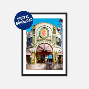 May include: A framed digital download print of a vintage building with the word "PRATER" in a circular sign. The building has a light beige facade with green and red accents, and a pink awning. A Ferris wheel is visible in the background.