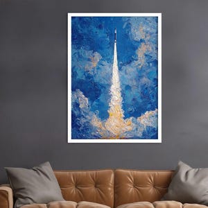 May include: An abstract painting of a rocket launching into a blue sky with white and yellow clouds. The artwork is framed in white and hangs on a dark grey wall above a brown leather sofa.