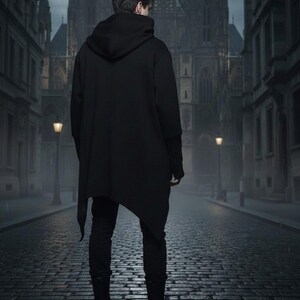 K&ouml;nnte beinhalten: Eine Person in einem schwarzen Kapuzenmantel mit asymmetrischem Saum, schwarzer Hose und Stiefeln steht auf einer Kopfsteinpflasterstra&szlig;e. Im Hintergrund befinden sich ein Geb&auml;ude im gotischen Stil und Stra&szlig;enlaternen, was eine dunkle, atmosph&auml;rische Szene erzeugt.