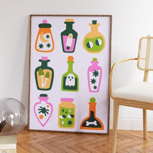May include: A framed print featuring nine colorful potion bottles with various designs. The bottles are in shades of orange, green, and pink, with illustrations of moons, stars, mushrooms, ghosts, and other whimsical elements. The artwork has a playful, cartoonish style.