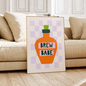 Peut inclure: Une affiche encadrée représentant une bouteille orange stylisée avec un bouchon vert sur un fond à carreaux lavande et blanc. Les mots "BREW BABE" sont imprimés en vert sur un rectangle rose sur la bouteille.