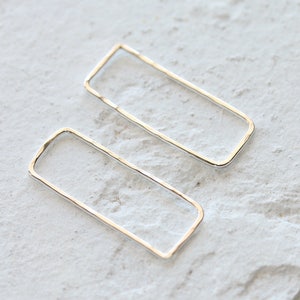 Pode incluir: Um par de brincos retangulares de prata. Os brincos são simples e minimalistas.