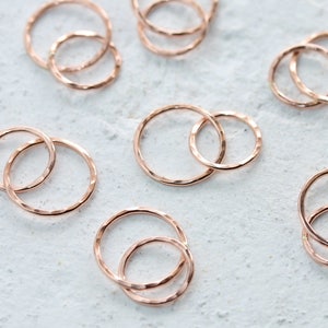 May include: A set of 10 rose gold hammered metal rings. The rings are in various sizes and are stacked on top of each other.