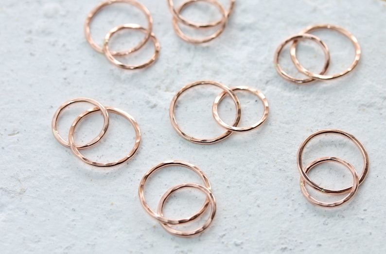 May include: A set of 10 rose gold hammered metal rings. The rings are in various sizes and are stacked on top of each other.