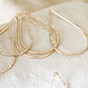 May include: A set of four gold teardrop-shaped hoop earrings. The earrings are made of hammered metal and have a slightly irregular shape.