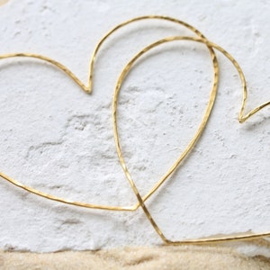Può includere: Due cerchi dorati a forma di cuore, uno leggermente più grande dell'altro, sono esposti su una superficie bianca testurizzata.
