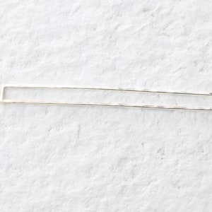 May include: A silver, hammered, rectangular bar with rounded edges. The bar is a simple, minimalist design.