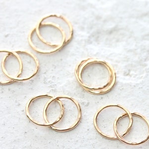 May include: Set of five gold-toned rings, each ring is a double ring, with one ring slightly larger than the other. The rings are arranged in a scattered pattern on a white surface.