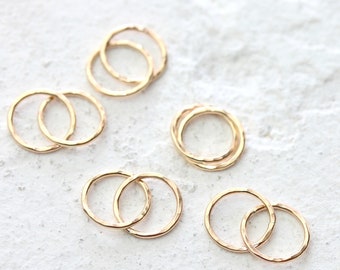 May include: Set of five gold-toned rings, each ring is a double ring, with one ring slightly larger than the other. The rings are arranged in a scattered pattern on a white surface.