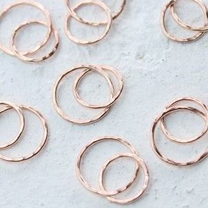 May include: A set of eight rose gold hammered metal rings. The rings are in various sizes and are stacked on top of each other.