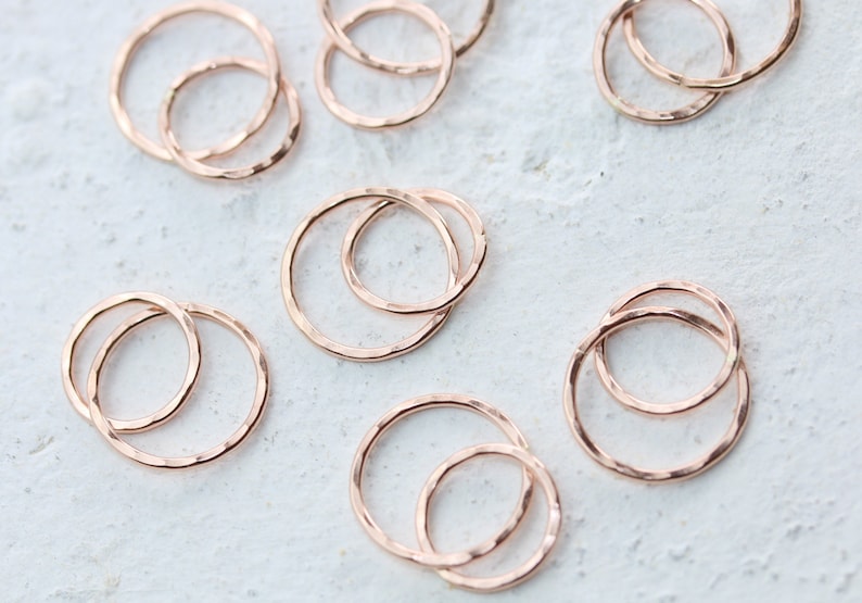 May include: A set of eight rose gold hammered metal rings. The rings are in various sizes and are stacked on top of each other.