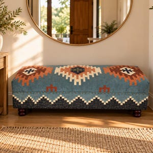 May include: A rectangular upholstered bench featuring a blue fabric base with a geometric pattern in shades of rust, cream, and dark navy. The bench is supported by four dark brown turned wooden feet and includes a row of decorative metal nailhead trim.
