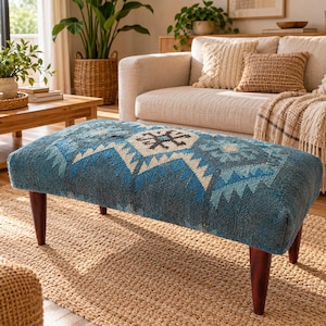 Può includere: Un pouf rettangolare rivestito in tessuto blu testurizzato con un motivo geometrico nei toni dell'azzurro, del blu scuro e del crema. Il mobile è sostenuto da quattro gambe affusolate in legno marrone scuro per una base stabile.