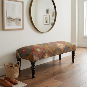 Può includere: Panca imbottita con un colorato motivo geometrico nei toni del rosso, arancione, verde e blu. La panca ha gambe in legno scuro ed è posta contro un muro bianco con uno specchio rotondo e opere d'arte incorniciate. Un cestino intrecciato e scarpe sono in primo piano.