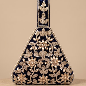 Puede incluir: Un bolso de mano triangular de terciopelo azul marino con bordados metálicos dorados en motivos florales, acentuado con cristales facetados transparentes y un borde de pequeñas perlas blancas. Incluye un asa vertical con bordado.