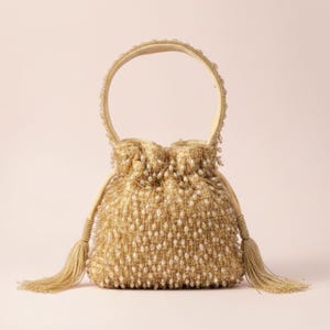 May include: A gold-toned drawstring handbag featuring an intricate mesh exterior adorned with numerous small, clear beads. The bag includes a single circular top handle and two long, decorative tassels hanging from the sides of the drawstring closure.