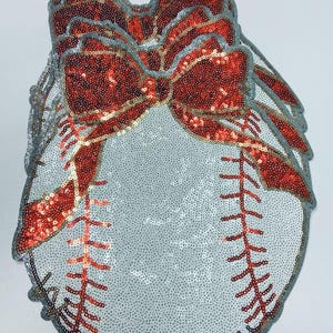 May include: A collection of baseball-themed decorations. Each piece is covered in silver sequins, with red sequined bows and stitching. The edges are trimmed with a silver border. The baseball stitching is red.
