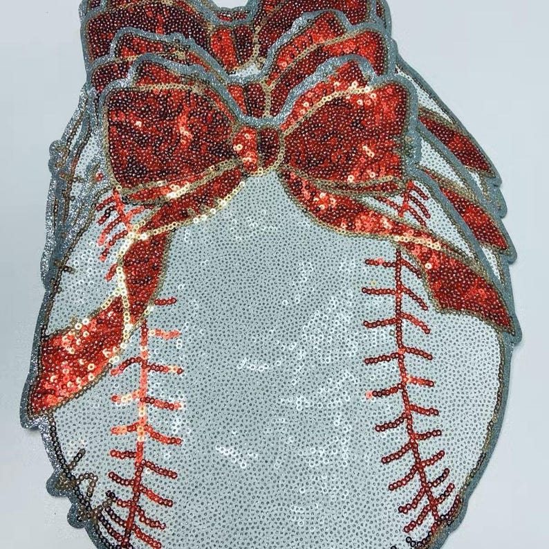 May include: A collection of baseball-themed decorations. Each piece is covered in silver sequins, with red sequined bows and stitching. The edges are trimmed with a silver border. The baseball stitching is red.