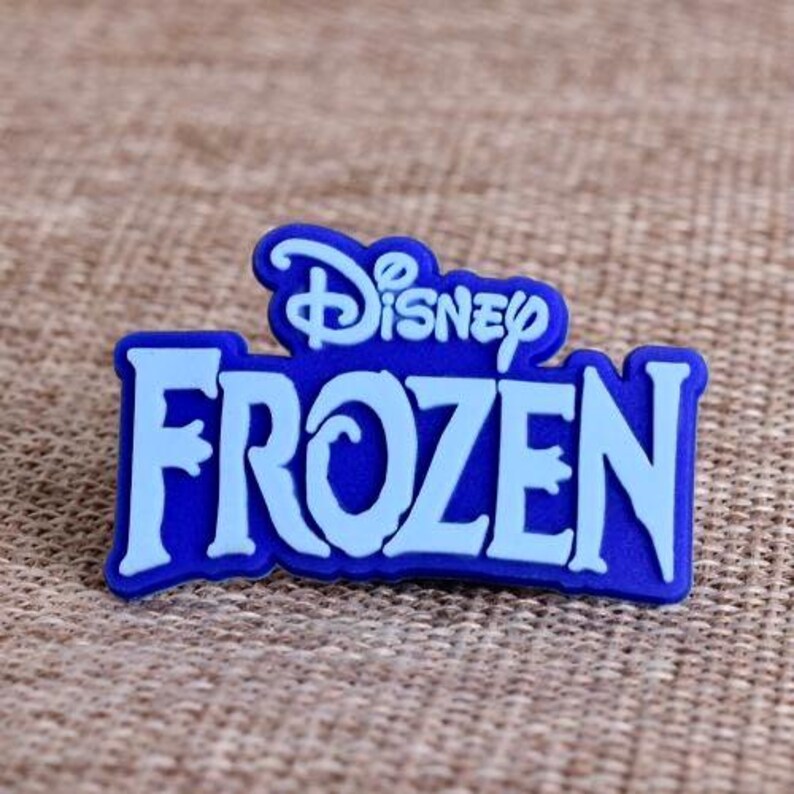 May include: A blue and light blue Disney Frozen logo. The word "Frozen" is in light blue, with the Disney logo above it in a darker blue. The logo is on a textured, tan surface.