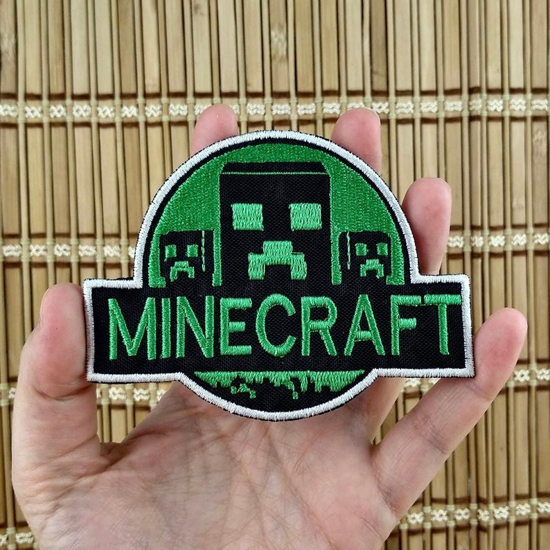 K&ouml;nnte beinhalten: Ein Minecraft-Aufn&auml;her mit gr&uuml;nem und schwarzem Design. Der Aufn&auml;her zeigt das Wort "MINECRAFT" in wei&szlig;en Buchstaben auf schwarzem Hintergrund. Der Aufn&auml;her hat einen gr&uuml;nen kreisf&ouml;rmigen Rand mit einem schwarzen pixeligen Charakter.