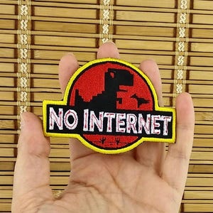 K&ouml;nnte beinhalten: Ein schwarzer, roter und gelber Aufn&auml;her mit dem Text "NO INTERNET". Der Aufn&auml;her zeigt eine Dinosaurier-Silhouette in einem roten Kreis, &auml;hnlich einem Filmlogo. Der Aufn&auml;her wird in einer Hand gehalten.