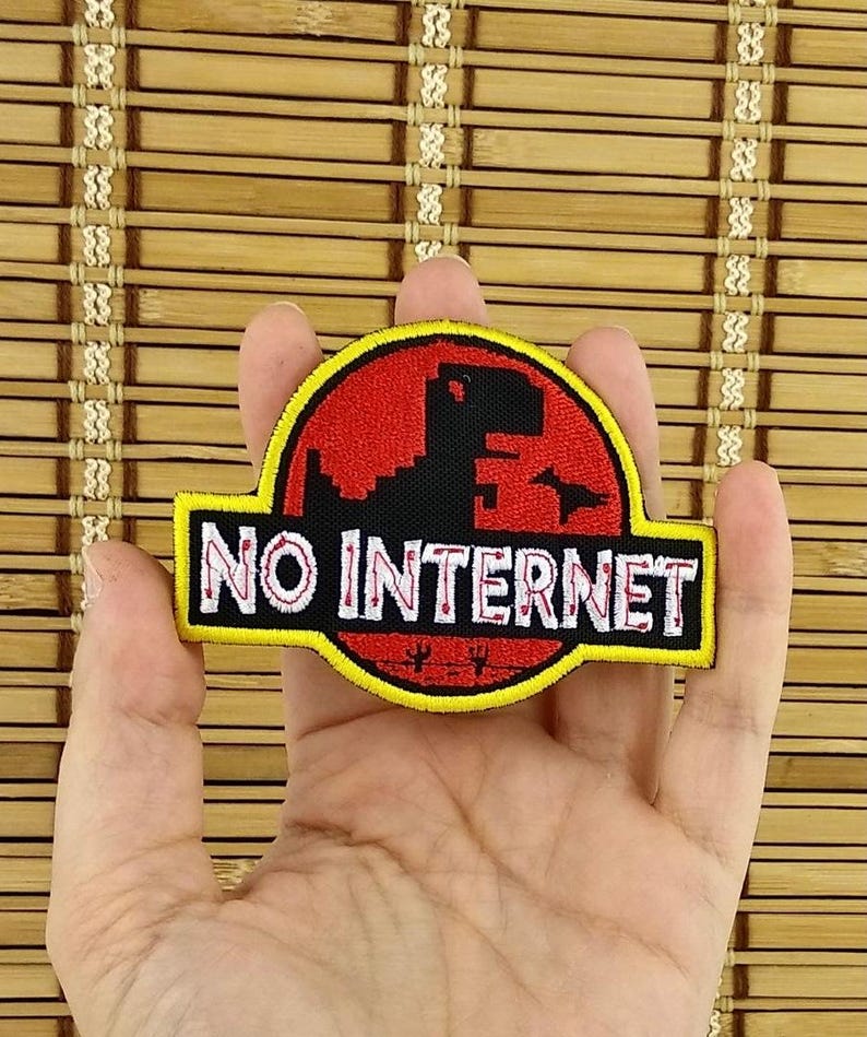 K&ouml;nnte beinhalten: Ein schwarzer, roter und gelber Aufn&auml;her mit dem Text "NO INTERNET". Der Aufn&auml;her zeigt eine Dinosaurier-Silhouette in einem roten Kreis, &auml;hnlich einem Filmlogo. Der Aufn&auml;her wird in einer Hand gehalten.
