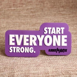 May include: A purple rectangular magnet with the words "EVERYONE STRONG. START" in white, bold letters. The hashtag "#JUSTMERIT" is in the lower right corner. The magnet is on a textured, tan surface.