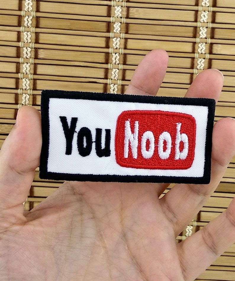 K&ouml;nnte beinhalten: Gestickter Aufn&auml;her mit den Worten "You Noob" in Schwarz und Wei&szlig; auf wei&szlig;em Hintergrund, mit einem roten Rechteck. Der Aufn&auml;her hat einen schwarzen Rand.