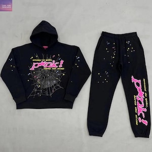 Op de afbeelding: Zwarte hoodie en joggingbroek set. De hoodie heeft een roze spinnenweb ontwerp met de tekst "pank!" en "nevermind the spider, heres the slime". De joggingbroek heeft dezelfde tekst op de broekspijp en verspreide sterren.