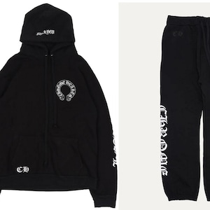 May include: Black hoodie and joggers set. The hoodie has a hood with text, a front pocket, and a white logo on the chest. The sleeves have white text. The joggers have a drawstring waist and a white logo. The set is made of a soft material.