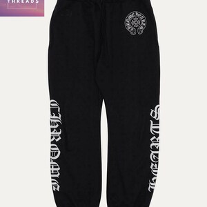 May include: Black sweatpants with a drawstring waist and white lettering down the sides. The text reads "CHROME HEARTS" and a circular logo is visible on the upper right leg. The upper left corner of the image has the text "TOP TEN THREADS".
