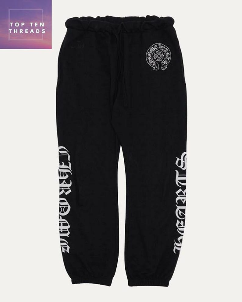 May include: Black sweatpants with a drawstring waist and white lettering down the sides. The text reads "CHROME HEARTS" and a circular logo is visible on the upper right leg. The upper left corner of the image has the text "TOP TEN THREADS".