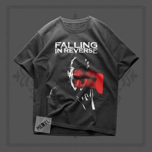 May include: Dark gray t-shirt with the text "FALLING IN REVERSE" in white. The shirt features a graphic of a person's face with red accents and a hand gesture. The brand name "MERYL" is in the bottom left corner.