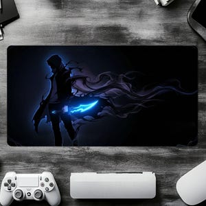 May include: A rectangular gaming mousepad featuring a dark illustration of a character with a glowing blue weapon and flowing dark energy. The design is set against a dark blue background. The mousepad is surrounded by gaming accessories.
