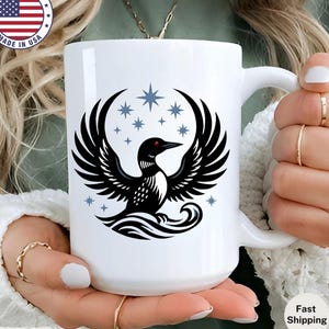 May include: White ceramic mug featuring a black and white bird design with outstretched wings and a red eye, surrounded by blue stars. The mug has a curved handle and the text "Made in USA" on the side. It is a 15 oz mug.