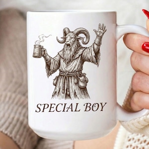 以下が含まれることがあります： 白いセラミックマグカップ。黒いイラストは、マグカップを持ち、手を挙げているヤギのような姿です。「SPECIAL BOY」の文字が下に印刷されています。マグカップには大きなハンドルが付いています。