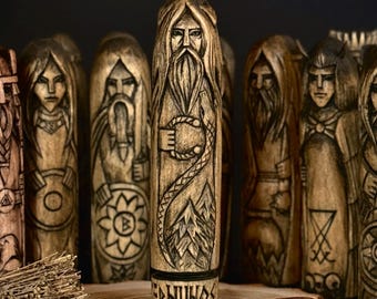 May include: A collection of intricately carved wooden figures, each depicting a stylized human form with detailed facial features and clothing. The central figure is labeled "ERNUHOS". The figures are arranged on a wooden slice, with several small, round, reddish-brown objects in front.