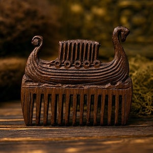 May include: A dark brown wooden hair comb featuring a carved relief of a Viking longship on the top handle. The ship design includes a curved prow and stern, a central structure, and circular shield details along the side of the vessel hull.