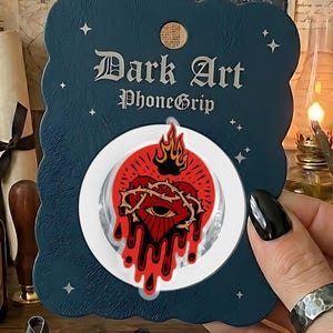 May include: A dark blue phone grip with the text "Dark Art PhoneGrip" and a red heart design with a crown and dripping blood. The image also shows various items like potion bottles, crystals, and a mug.
