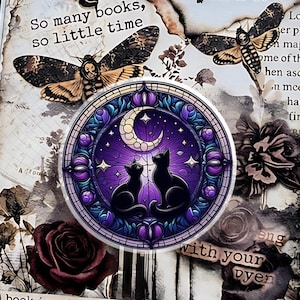 May include: A decorative book with a gothic theme. The cover features moth and butterfly illustrations, a circular design with two black cats under a crescent moon, and the text "So many books, so little time". A key with a skull charm hangs from the book.