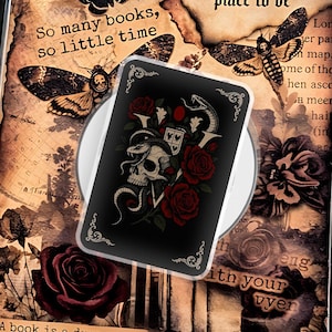 May include: A decorative book-shaped box with a vintage aesthetic. The box features butterfly and rose illustrations, along with the phrases "So many books, so little time" and "Between the pages of a book is a lovely place to be." A card with a skull and roses rests on top.