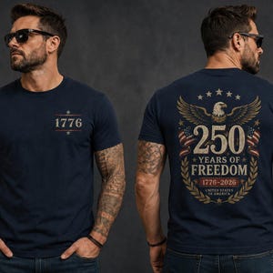 May include: A navy blue short-sleeve t-shirt featuring the text 1776 on the front chest. The back displays a graphic of a bald eagle, American flags, and the text 250 YEARS OF FREEDOM 1776-2026 UNITED STATES OF AMERICA in gold and white.