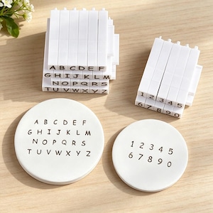 May include: A set of white rectangular stamps featuring black letters A through Z and numbers 0 through 9, accompanied by two white circular plates displaying the same alphabet and numerical sequences in black ink for clear identification.
