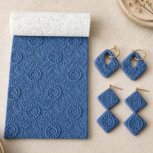 May include: A white cylindrical patterned texture roller next to a rectangular blue clay sheet with a matching embossed floral design, accompanied by two pairs of blue diamond-shaped clay earrings featuring gold-toned metal hardware components.