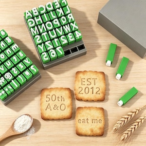 Puede incluir: Un juego de sellos de goma verdes con letras, números y símbolos blancos en bandejas grises. Tres galletas cuadradas están impresas con el texto EST 2012, 50th A & O y eat me. Se incluyen una cuchara de madera con polvo blanco y espigas de trigo.