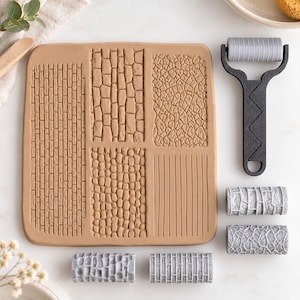 Puede incluir: Una placa de textura de arcilla cuadrada de color tostado con cuatro patrones en relieve distintos que incluyen ladrillo, piedra, tierra agrietada y líneas verticales, junto a un rodillo con mango negro y cinco rodillos grises.